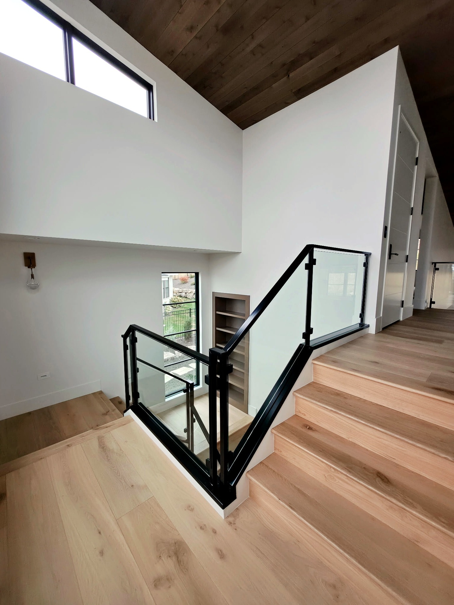 Hillside Haven upper stair landing — black glass railing, wood ceiling, and professionally painted walls